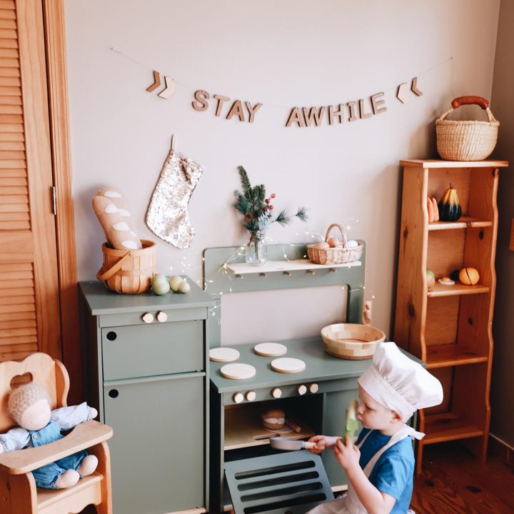 A little chef at a wooden play kitchen under a Stay Awhile banner