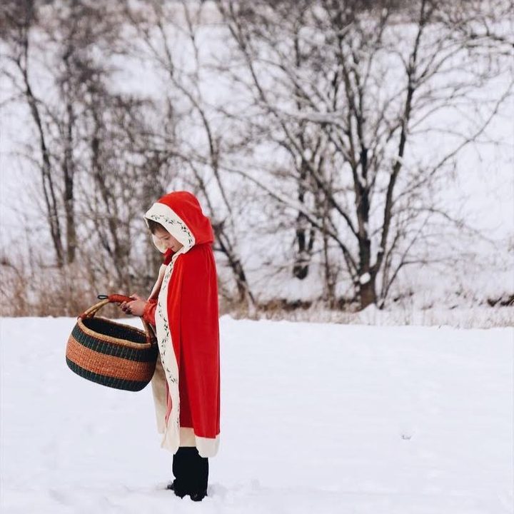 A child in a red cloak carrying a basket through the snow